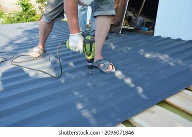 A roofing contractor is installing metal roof panels, screwing metal roofing sheet to the roof deck using an electric screwdriver. 