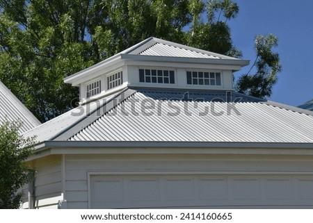 ROOFLINE WITH GABLED ANGLES AND A FEATURED LIGHTWELL ON TOP - Architectural style silver  metal roof with a windowed light well turret crows nest above and a gray timber panel lift garage door below
