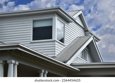 ROOFLINE WITH VARIOUS MULTI ANGLED GABLED CORREGATED IRON ROOFING with gutters, flat patio verandah roof thick columns on a large architectural white wooden siding weatherboard character style house