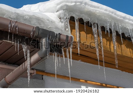 The roofs of the buildings are covered with snow and ice after a big snowfall. Huge icicles hang from the facades of buildings. Melting icicles in the rays of the spring sun.