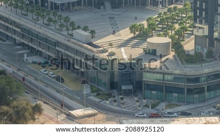 Rooftop garden with palms near entrance to office towers in financial district of Dubai city evening timelapse. Aerial view with road and parking