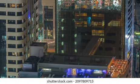 Rooftop Swimming Pool Viewed From Above Night Timelapse. Aerial Top View At Financial District With Illuminated Skyscrapers. People Relaxing. Dubai, UAE