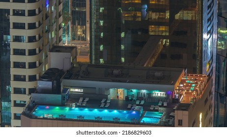 Rooftop Swimming Pool Viewed From Above Night Timelapse. Aerial Top View At Financial District With Illuminated Skyscrapers. People Relaxing. Dubai, UAE