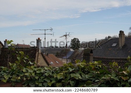 The rooftops of old residential houses with chimneys and analog antennas. On the foreground there is a defocused ivy hedge. Blue sky is on background with some white clouds with a lot of copy space. Stock photo © 