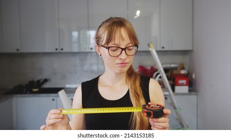 Rookie Blue Collar Worker Woman Looking At A Tape Measure. Young Female Creator Using A Tape Measure. Indoor Shot. High Quality Photo