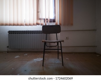 Room In An Abandoned Building With Office Equipment. An Old Dirty Office With A Worn Out And Torn Office Chair And Cobwebs All Around. Open Window With A Wooden Frame Behind The Drawn Strip Curtains.