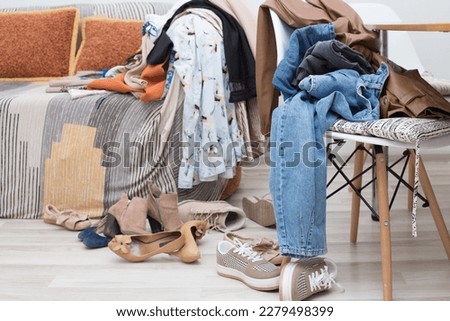 room in the apartment with furniture, sofa, chair. There are a lot of women's clothes on the sofa, dresses, jeans, shoes on the chair and on the floor. Conscious use of materials, cleaning, declutteri