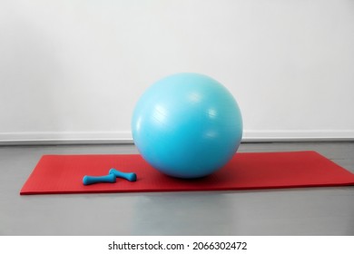 In The Room, A Blue Dumbbell Sports Ball And A Red Yoga Mat Lie Against The Wall.