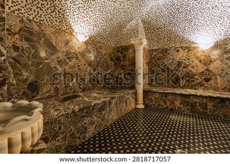 The room features marble walls and a patterned floor. There is a large fountain and benches made of marble. Soft lighting creates a warm atmosphere in the wellness center.