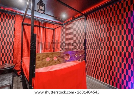 room featuring a four-poster bed with red curtains and a geometric red and black patterned wall.