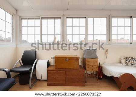 A room full of unconnected junk with trunks and a bed under a bay window with French-style white aluminum windows