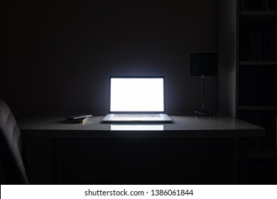 Room illuminated by a computer screen at night, no people. Empty workplace lit by a laptop display in the darkness, late work, overtime concept