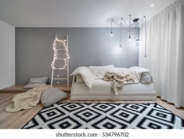 Room in a modern style with white and gray walls and a parquet with a carpet on the floor. There is a sofa, plaids, pillows, wooden ladder with sphere glowing lamps, hanging lamps and decorative owls.