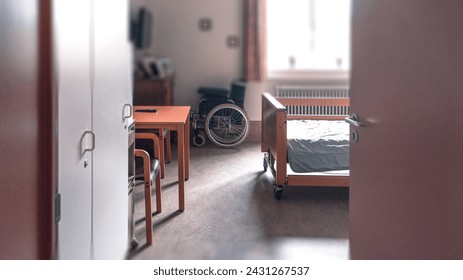 Room in a nursing home through an open door, part of a bed, table, chair, wheelchair, partial background blur. - Powered by Shutterstock