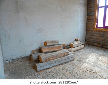 Room with plastered walls and a stack of old wooden logs on a gravel floor. Window letting in natural light. House renovation, historical building restoration concept.                  