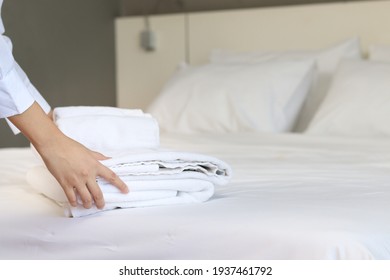 Room service maid cleaning and making bed hotel room concept, woman hands putting stack of fresh white bath towels on bed sheet.  - Shutterstock ID 1937461792