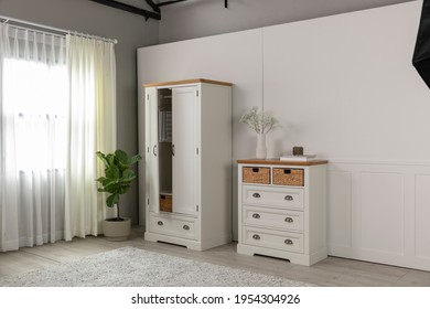 Room set in furniture photography studio featuring antique French provincial style wardrobe and chest of draws propped with plants and household items. Angle shot