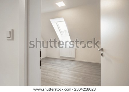 A room with a slanted ceiling and a skylight, light-colored laminate flooring, white walls, and an open door, showcasing a clean and modern interior.