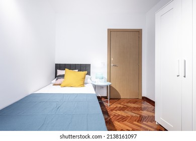 Room With White Wardrobe, Small Bed, Round Blue Nightstand And Mahogany Herringbone Parquet Flooring