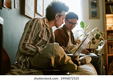 Roomies using laptops to write codes together while they sitting on single bed