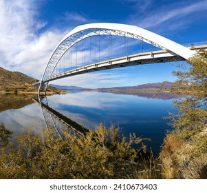 Roosevelt Bridge Arch Ellipse Reflected in Apache Trail Lake Calm Water.  Scenic Superstition Mountains Landscape Angle View, Arizona Southwest US
