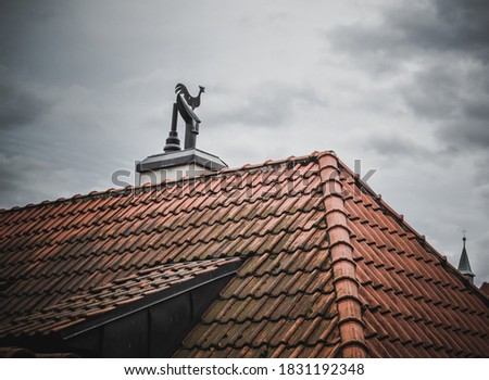 Rooster on the roof with red tiles and cloudy weather, Prague, Czech Republic