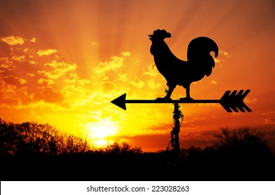 Rooster weather vane against sunrise with bright colors in clouds, concept for early morning wake up