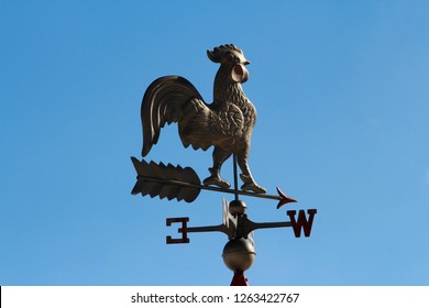 A rooster weather vane set against a cloudy blue sky  - Powered by Shutterstock