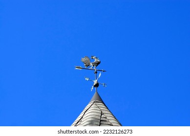 Rooster weathervane with compass points and arrow on clear blue sky.