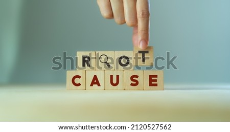 Root cause analysis concept. Define problems to find solution. Business problem solving.  Hand holds the wooden cubes with text ROOT CAUSE and magnifying glass icon on grey background,copy space. 