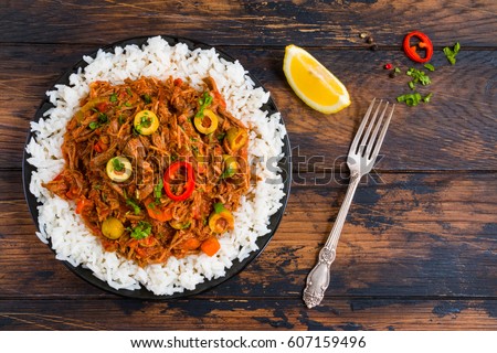 Ropa Vieja, Cuban national dish, stewed beef with wine and tomatoes on a black plate with a boiled rice. Wooden rustic table, top view.