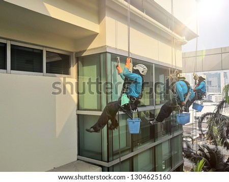 Rope access cleaning worker wearing safety harness hard hat working at height descending on rope performing washes a hospital complex glass wall.Safety at work. 