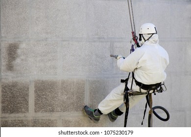 Rope access facade maintenance; A worker wearing a protective gear cleaning a stone exterior with sandblasting equipment