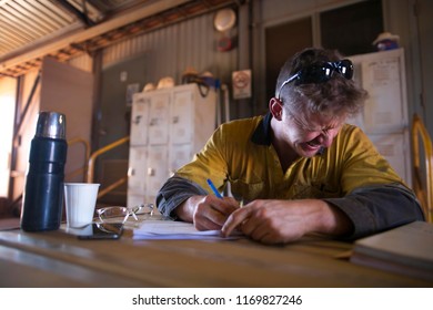 Rope Access Technician Male Miner Worker Setting On The Chair Yawning While Writing Job Hazard Analysis At Construction Site Perth, Australia 