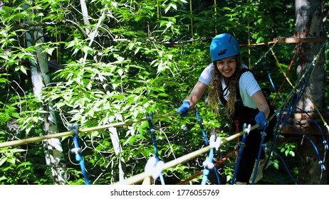 Rope adventure in forest - smiling woman walks on the rope bridge