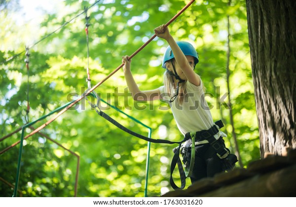 Rope adventure -\
a little girl walks on the rope bridge from the stand and holding\
by the ropes with her\
hands