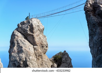 Rope bridge in mountains, cliffs of Mount Ai-Petri, Russia. It is tourist attraction of Crimea. View of high rope bridge between rocks against blue sky, scenery of hanging footbridge. Hiking theme. - Powered by Shutterstock