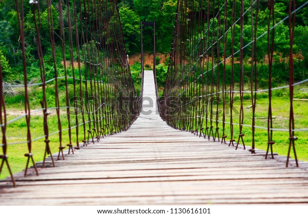 Rope bridge with wood planks\
across over the river and HouseBoat mountain forest in\
Thailand