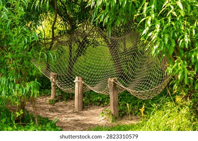 Rope hammock net stretched between wooden posts in lush green park. Outdoor relaxation area surrounded by trees, peaceful recreation, leisure and nature escape