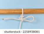 Rope knot Highpoint hitch, used to attach a rope to an object as a quick-release draw hitch tied around a wooden pole, view close-up on a blue background
