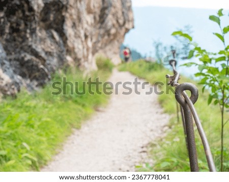 Rope and shackles anchored in hard dolomite limestone rock. Climbers path via ferrata. Iron chain and ropes fixed in block. Way to mountains peak as typical in the Alps. Monument to the dead climbers