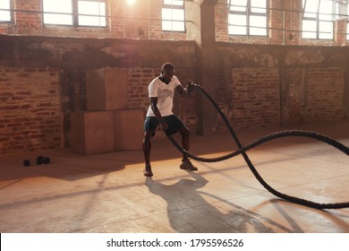 Rope workout. Sport man doing battle ropes exercise at gym. Black male athlete exercising, doing functional fitness training with heavy rope indoors 