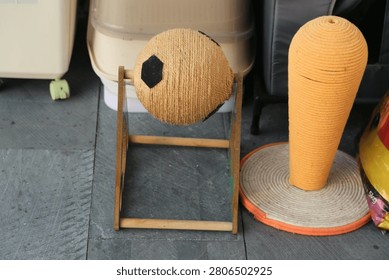 A rope-covered spherical training object is mounted on a small wooden stand next to a tall textured cylindrical item. The scene appears indoors or in a sheltered storage space with various household or training items arranged closely together.