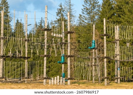 A ropes course stands in a clearing, surrounded by forest. outdoor adventure challenges for climbing and balance. Active leisure
