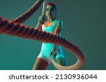 Ropes. Portrait of sportive woman workout, doing exercises with sports equipment isolated on green studio background in neon light. Sport, gym, action, motion, beauty concept. Fitness, hobby, health