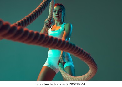 Ropes  Portrait sportive woman workout  doing exercises and sports equipment isolated green studio background in neon light  Sport  gym  action  motion  beauty concept  Fitness  hobby  health