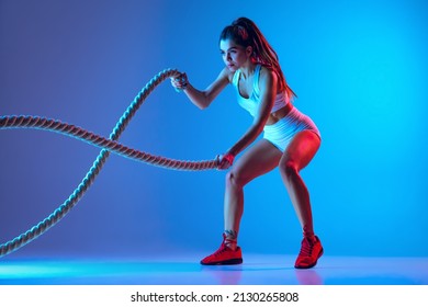 Ropes  Young sportive girl training and sports equipment isolated gradient blue  pink studio background in neon light  Female sport  action  motion  beauty concept  Fitness  healthy lifestyle