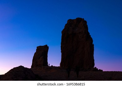 Roque Nublo, La Palmas De Gran Canaria/Spain - February 2020: The Impressive Roque Nublo Rock In Gran Canaria Island Shot At Dusk With A Hiker In The Middle Of Two Rocks