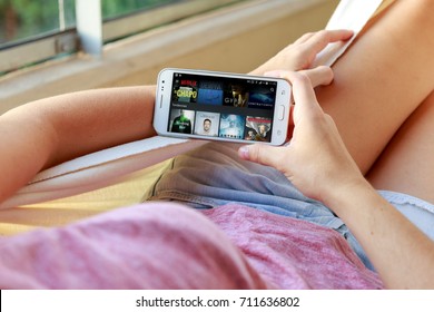 ROSARIO, ARGENTINA - JANUARY 19, 2017: Young woman in a hammock with a smartphone and Netflix´s menu on the screen. Millennial girl. Entertainment, movies, series. Application.