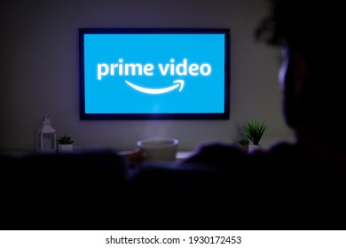 ROSARIO, ARGENTINA - MARCH 4, 2021: Amazon Prime video logo on the screen of led Smart TV. Afro man watching tv in home with a coffee cup in his hand..